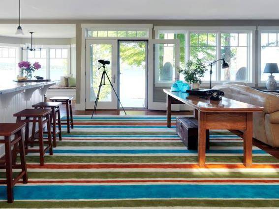 A room with a wall of glass windows, a white bar with brown bar stools and a green, red, blue and white striped carpet.