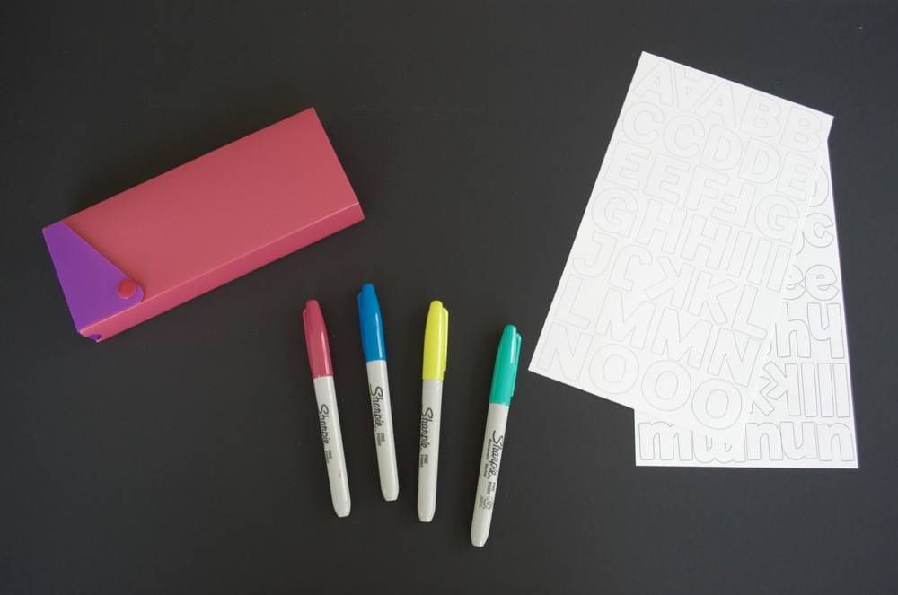Pink and purple pencil box laid out with four sharpies and white paper.