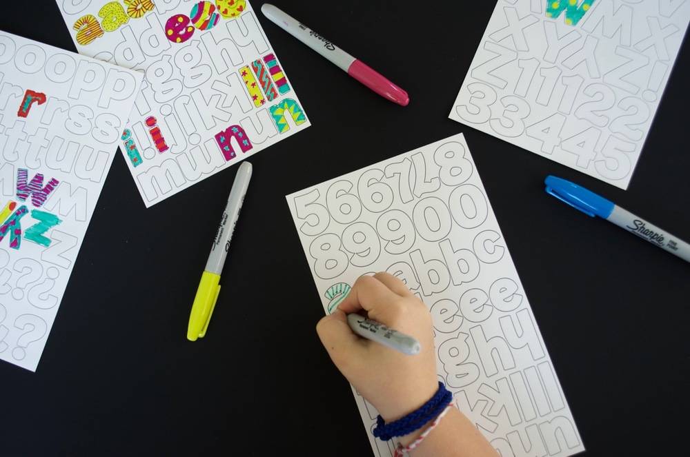 A person is using a permanent marker to color in a sheet of numbers and letters.