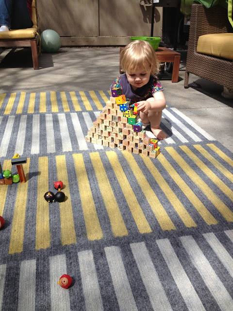 A tot sits among rugs.