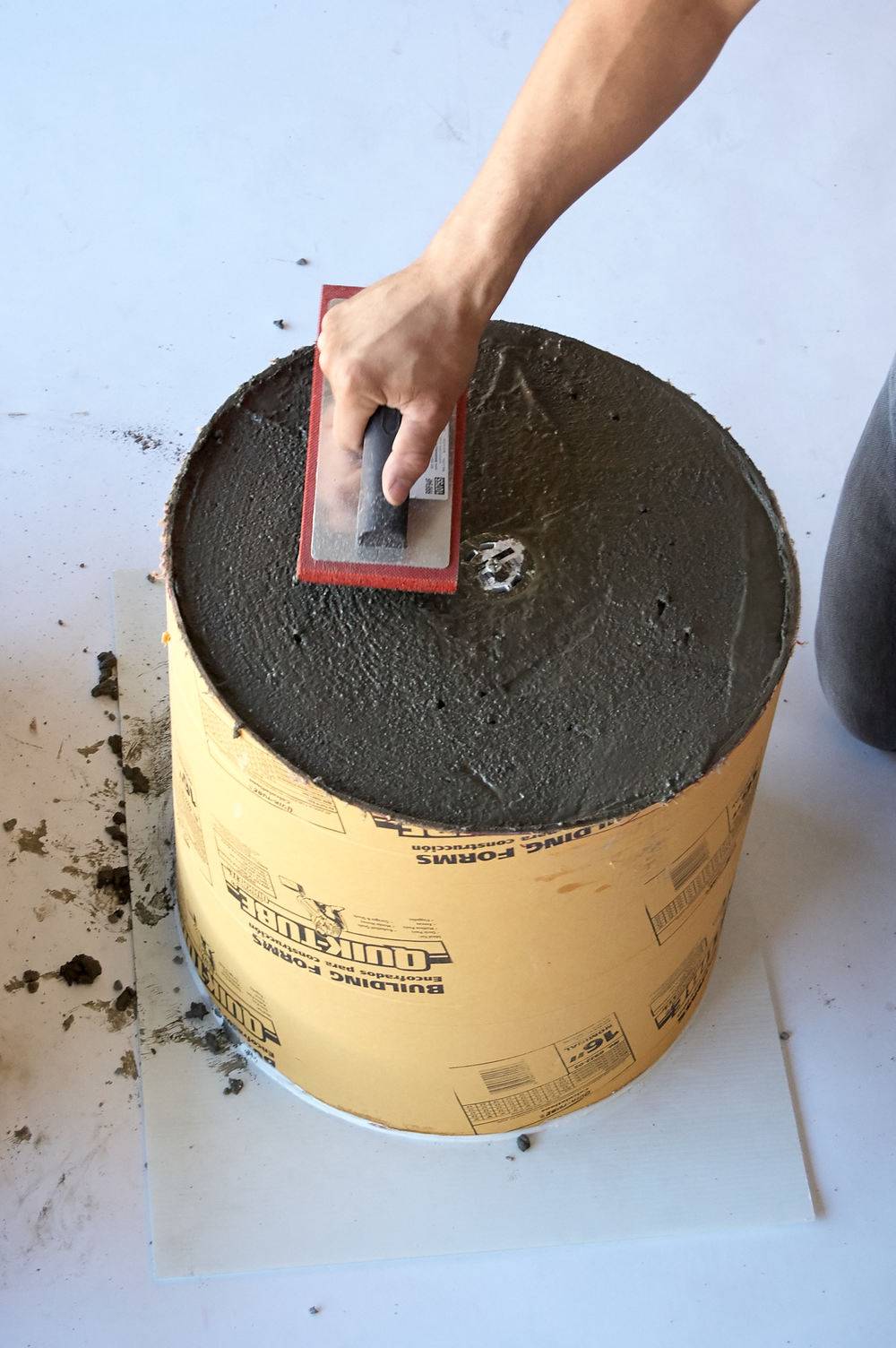 A person uses a trowel to flatten the surface and smooth the surface of concrete in a large container.
