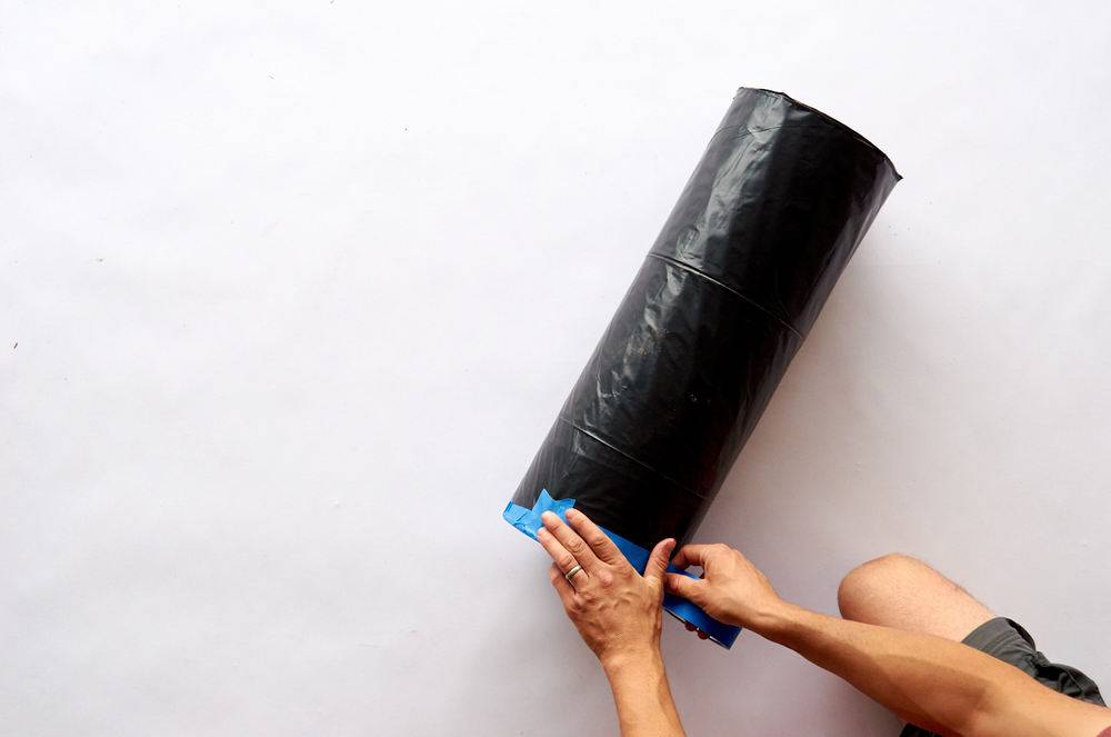A pair of man hands taping a roll of black plastic with blue tape.