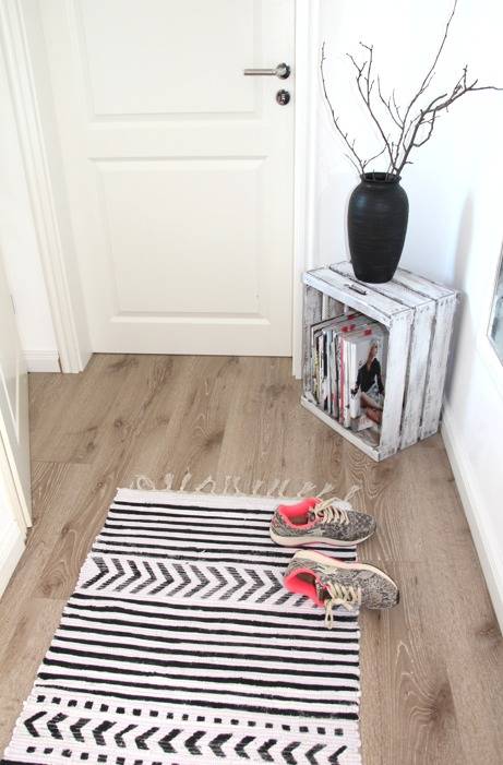 Two shoes lying on top of a rug on the wooden floor of a room.