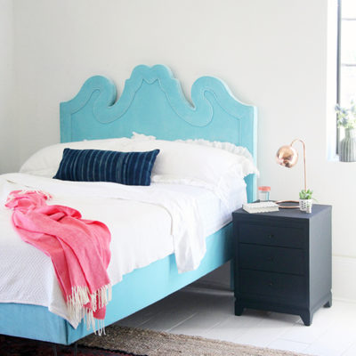 A simple room with a single blue bed flored with a rustic colored carpet.