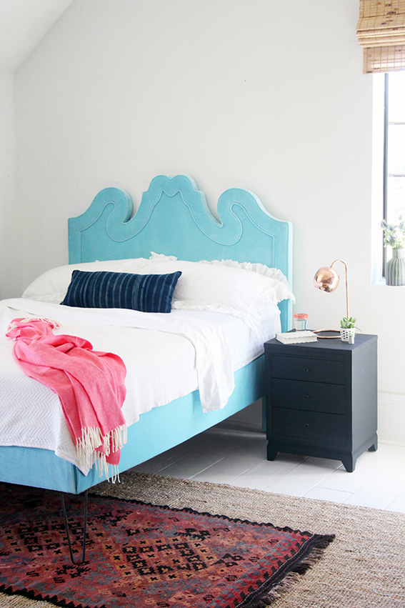 A simple room with a single blue bed flored with a rustic colored carpet.