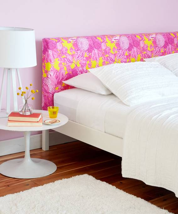 A white bed with a pink and yellow headboard has a nightstand next to it.