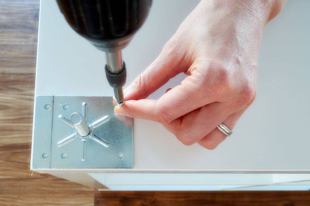 A person is screwing in a silver plate to a white surface.