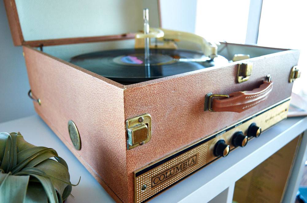 A suitcase-style record player with its lid open, sitting on a dresser while playing a record.