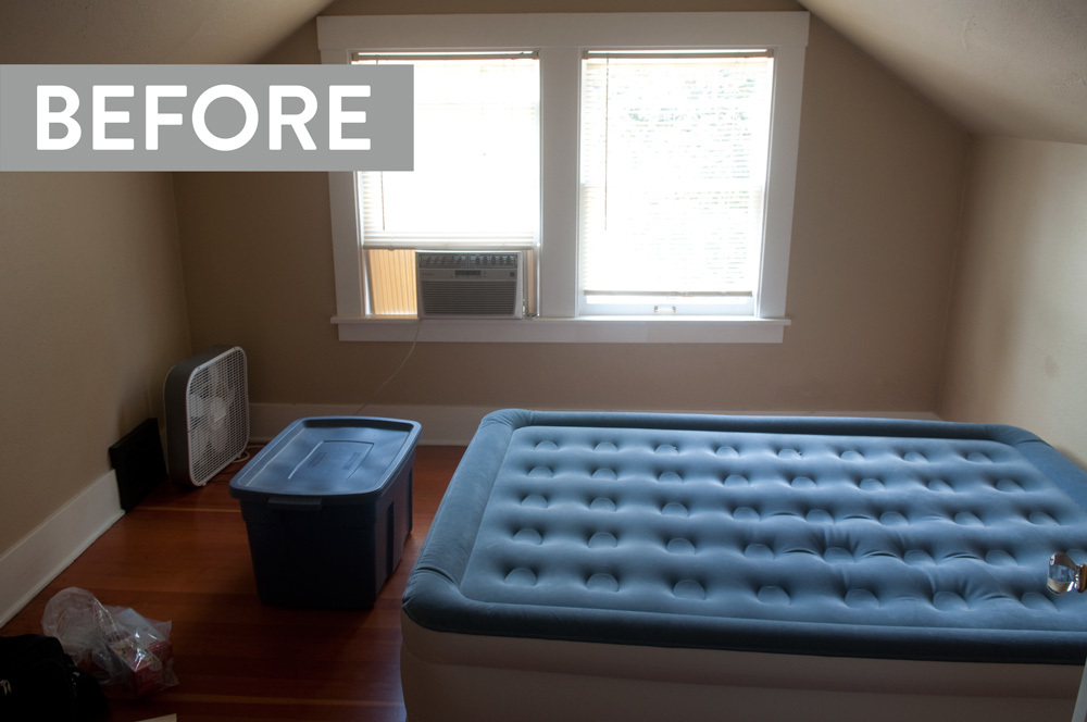 A blue tote sits in front of an air mattress in a room with a slanted ceiling.