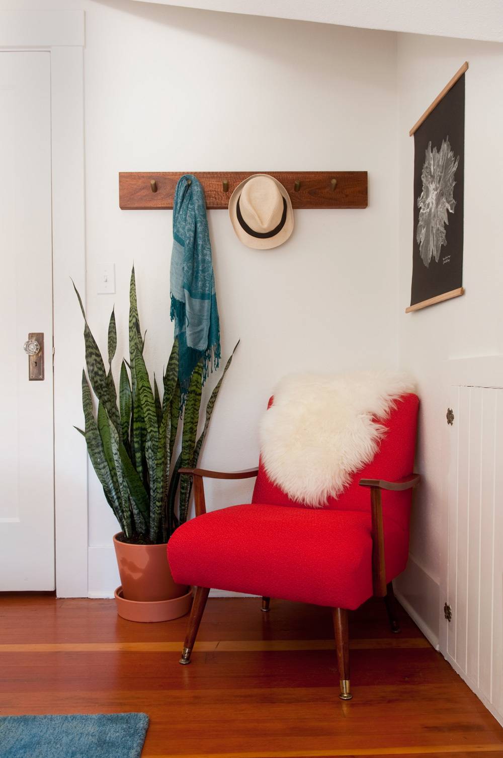 A red chair sits in the corner of a room near a plant.