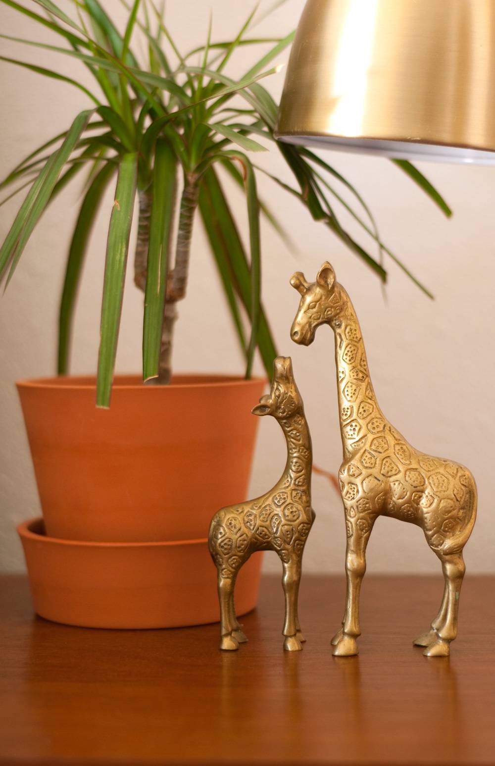 Two golden giraffe statues sit next to a potted plant on a wooden piece of furniture.