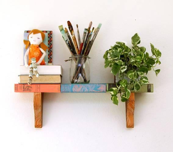 A small shelf has a plant, a pen jar and some books on it.