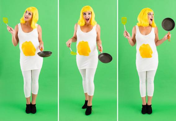 A lady in a white shirt with a yellow circle in the center designed to look like an egg holds a frying pan in front of a green screen.