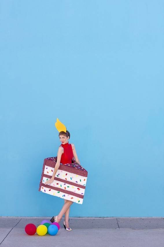 A person dressed like a piece of cake is walking in front of a light blue background.