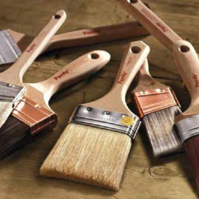 Seven paintbrushes of various sizes and bristle colors sit atop a wooden surface.