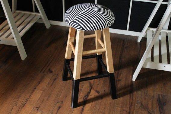 A wooden stool with black and white seat on it.