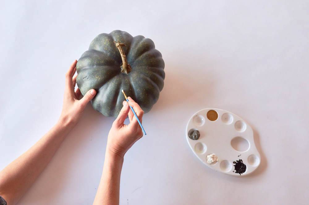 A woman painting a pumpkin with gray paint.