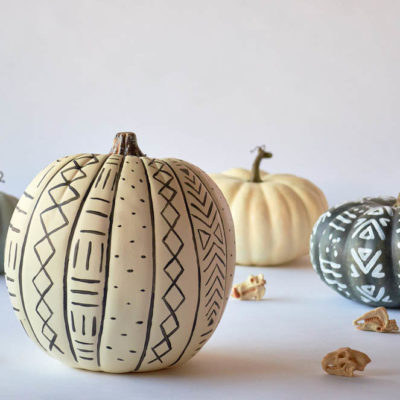 Four pumpkins painted white and gray, two of which with patterns and shapes.