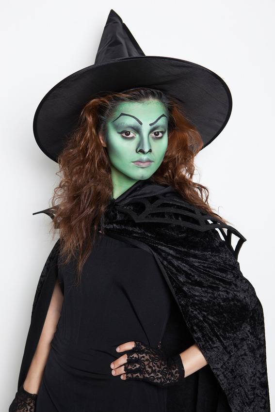 Woman dressed as a witch with green face and black lace gloves.