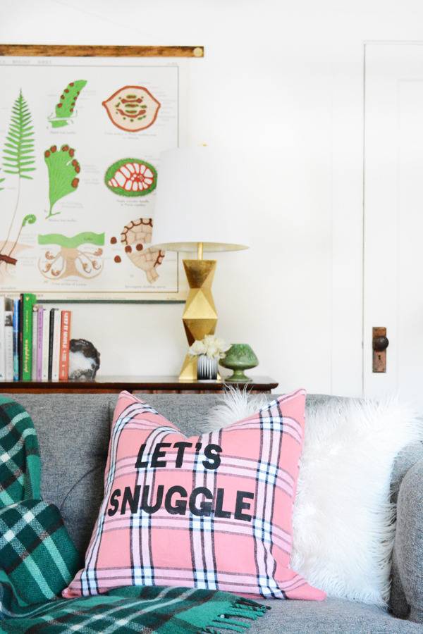 A pillow with the word Let's Snuggle sits on a couch.