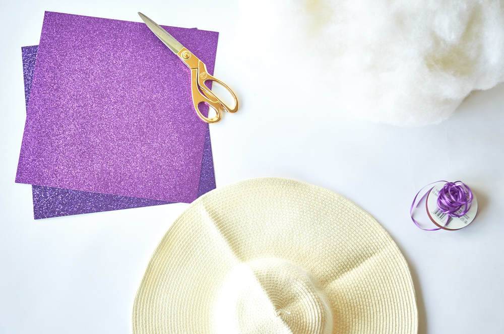 Two purple pieces of paper next to a beige hat and orange scissors on a white table