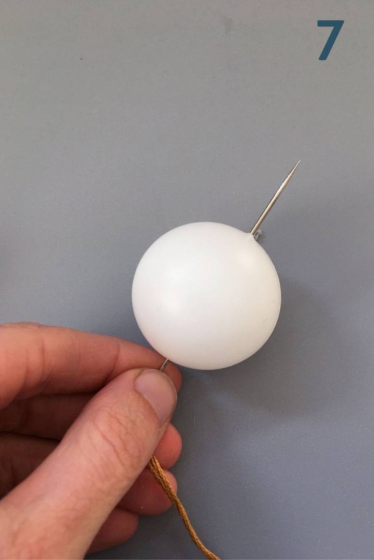 Woman holds a needle which has been pushed through a ping pong ball.