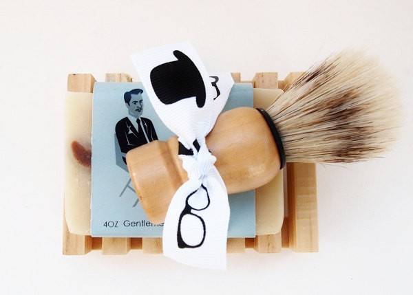 A white bow tie with glasses and a top hat image on it sits on top of a shaving cream brush.