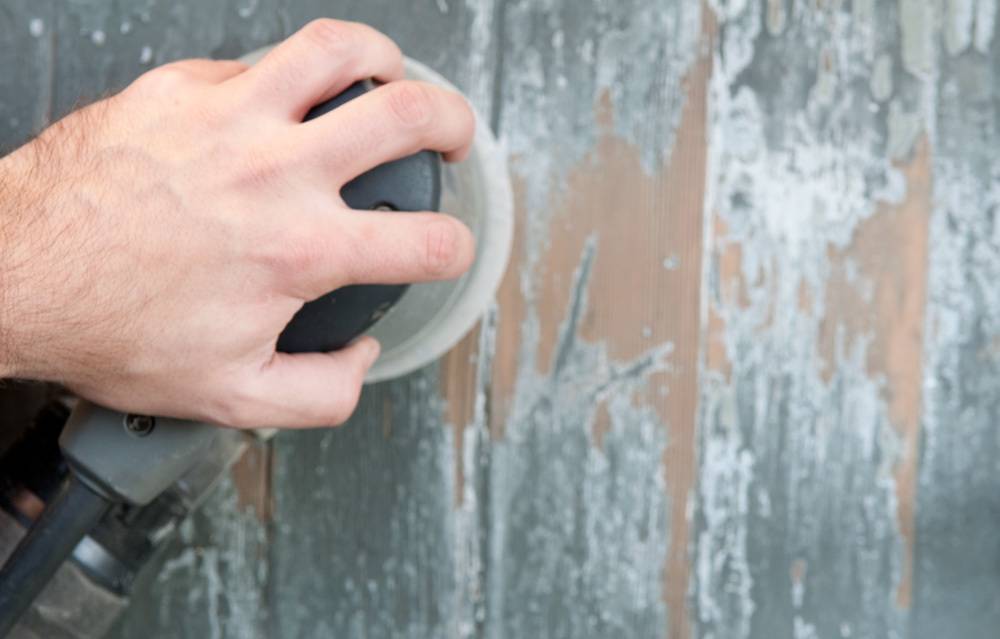 Man using a sander to remove old paint from wood.