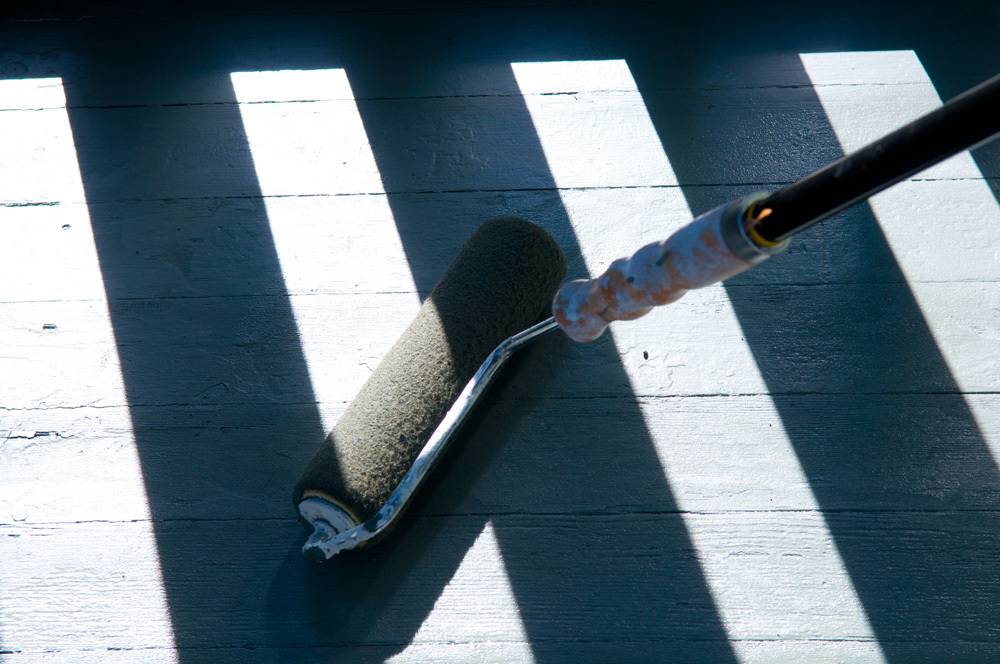 A person using a roller on a wooden deck.