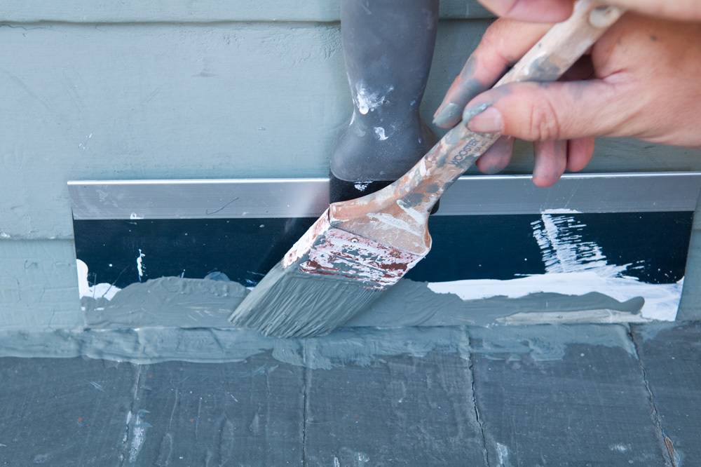 A person applying grey paint to a baseboard.