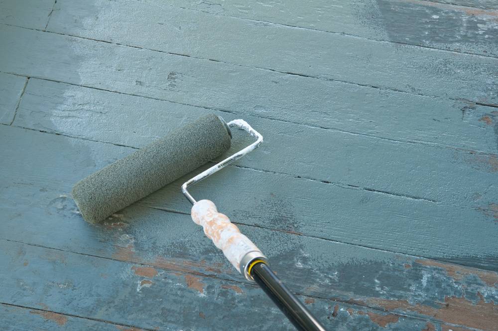 A person rolling grey paint on a wooden surface.