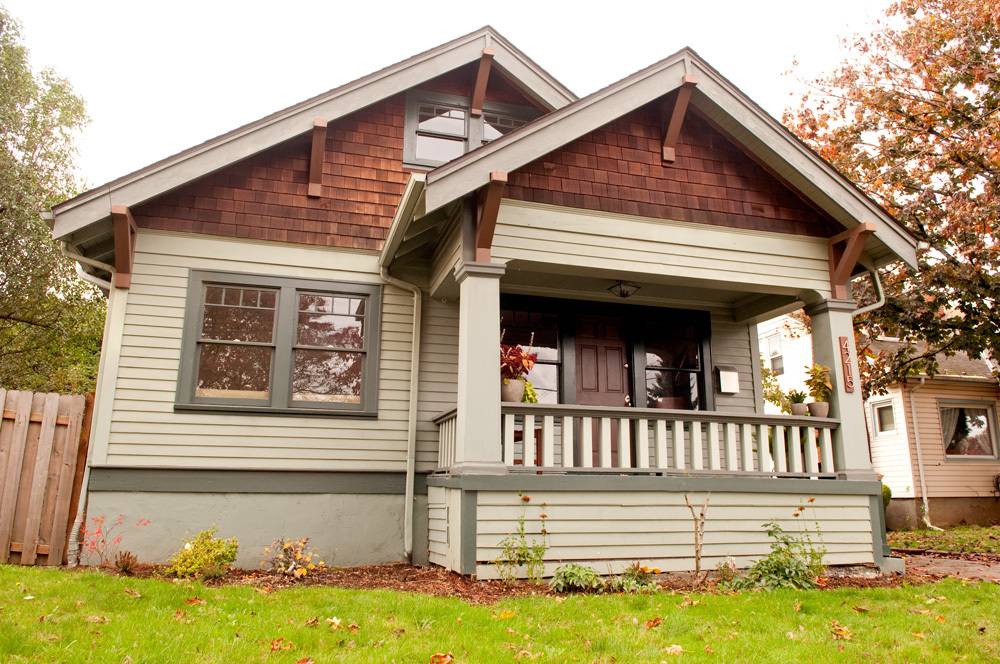 A dark red and beige brick and wood house with a lush green lawn in front.