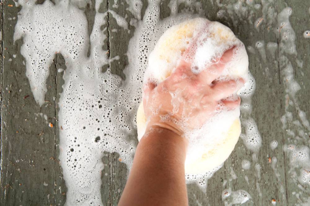 A hand holding a large soapy sponge on a soapy surface.