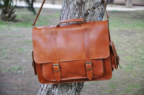 A brown leather purse hangs from a tree.