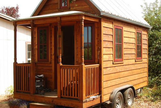 A wooden tiny house with a small porch on wheels.