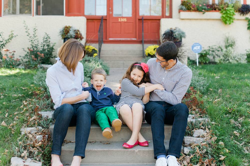 Two adults and two children are sitting on the steps in front of their home.
