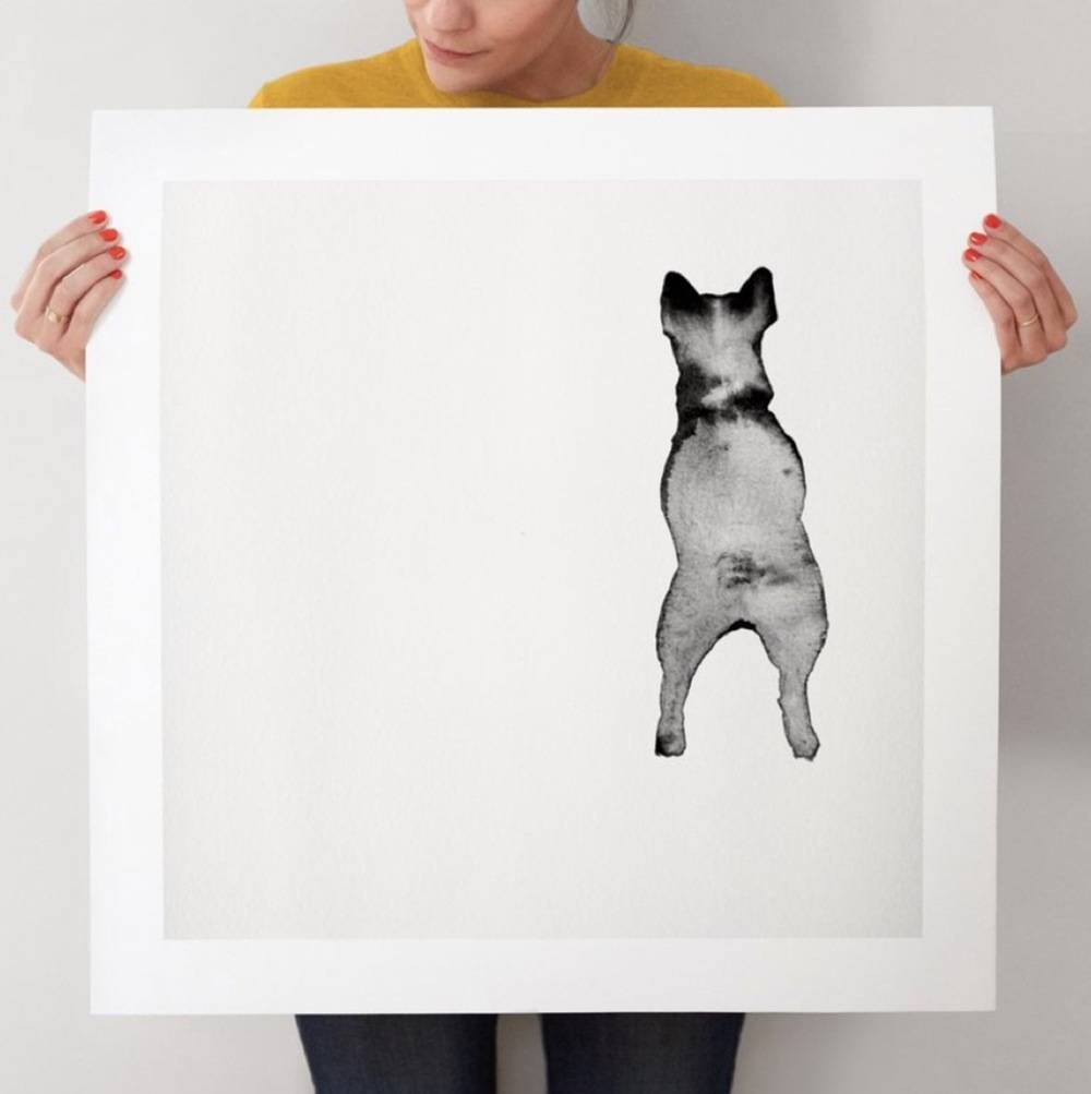 Woman holds up large black and white art print of a dog facing backwards.
