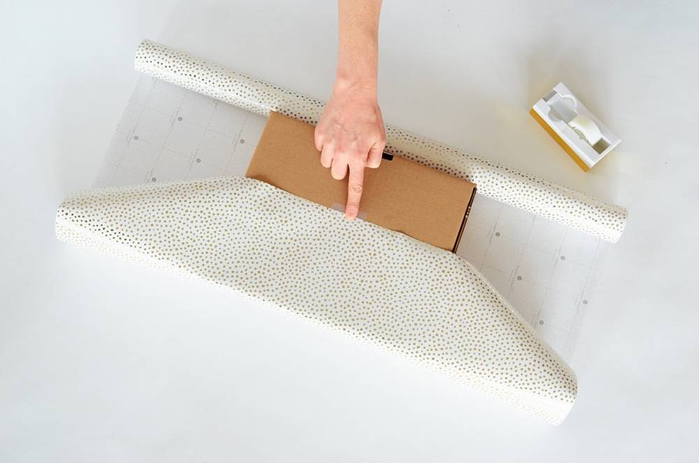 Person placing a cardboard box on the gift paper and ready to pack it.