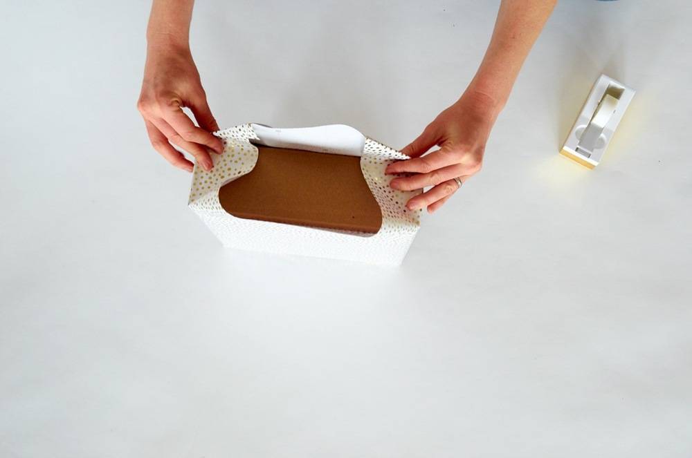 Two hands fold a white wrapping on a brown object.