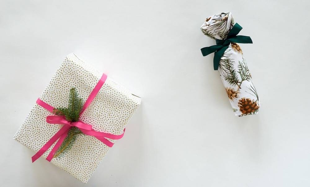 A white surfaces holds a white package with pink threads and another wrapped bottle shaped package.