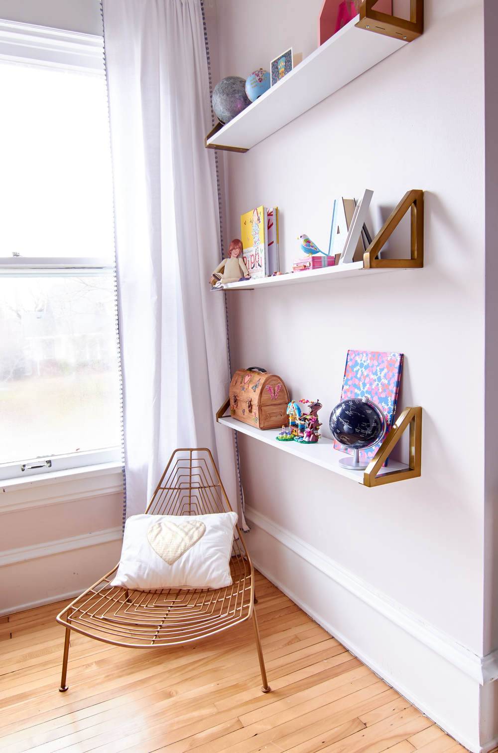 Young girl's bedroom with a small corner chair next to three bookshelves sitting on a wall.