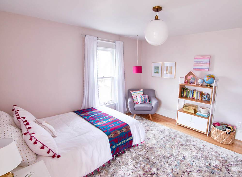 A bed is set up on a rug in a light pink room.