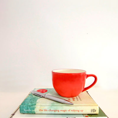 Red-orange coffee mug and a pen sitting atop a graduated stack of three books.