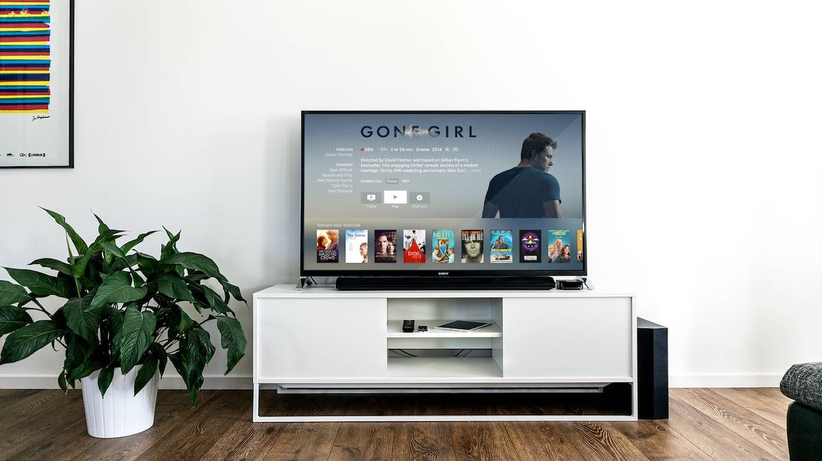 Large screen television sitting on top of a white entertainment center on a wooden floor next to a plant.