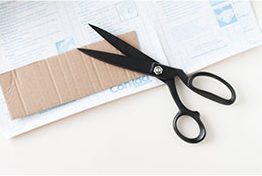 A pair of black scissors on top of some cardboard.
