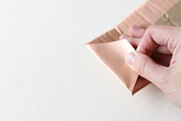 A person is folding paper over cardboard.