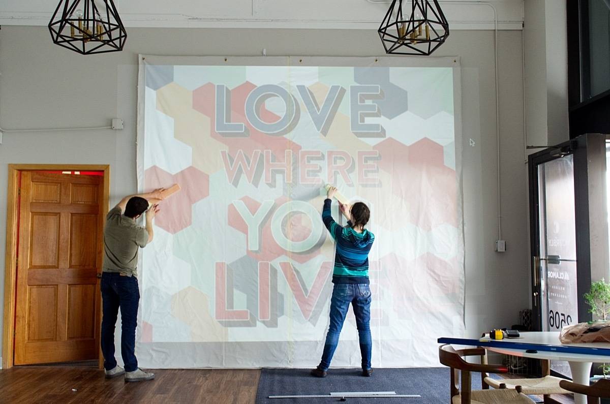 Two people measuring something on a banner that says LOVE WHERE YOU LIVE.