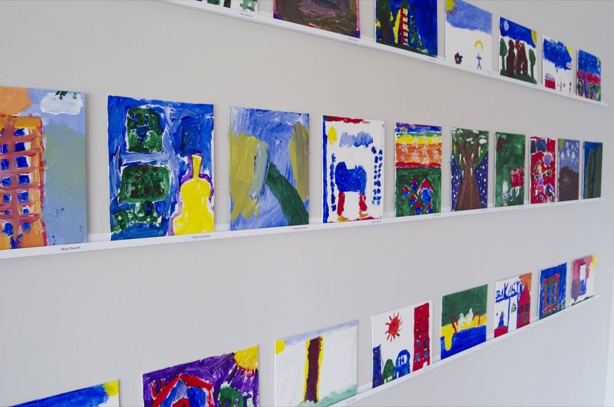 Colorful paintings are hanging in rows on a white wall.
