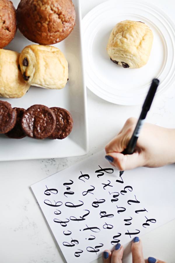 Plates of baked goods next to hand writing calligraphy letters.