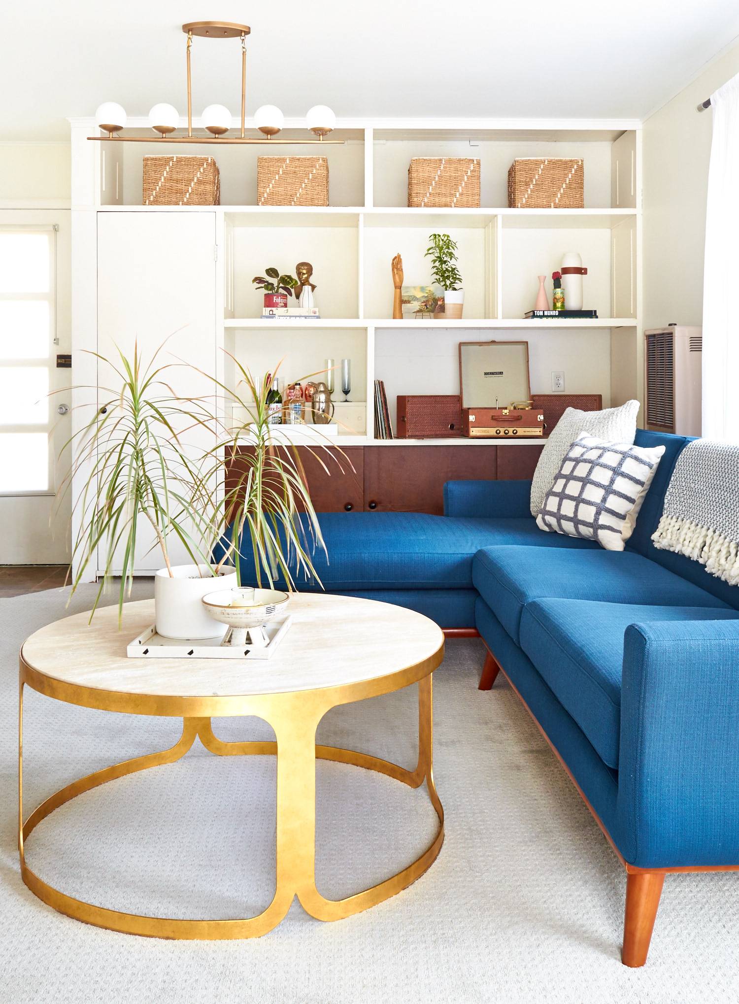 A clean living room with a blue couch, round coffee table and white shelf.
